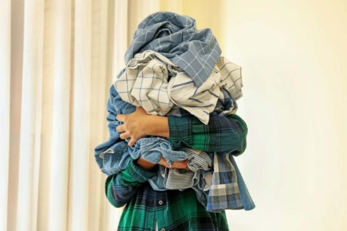 Persona con molti vestiti tra le braccia 