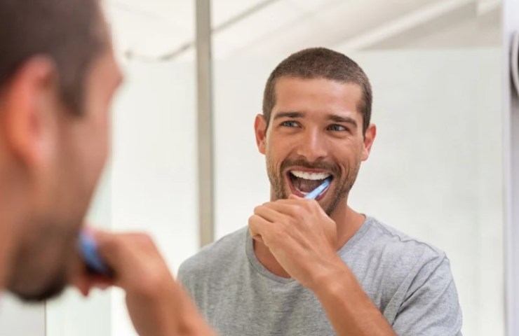 Uomo si lava i denti davanti allo specchio 