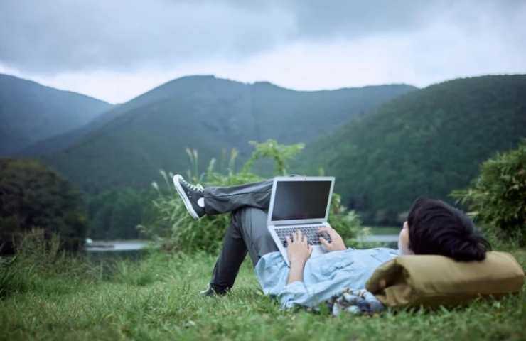 Uomo sdraiato sul prato con il pc 